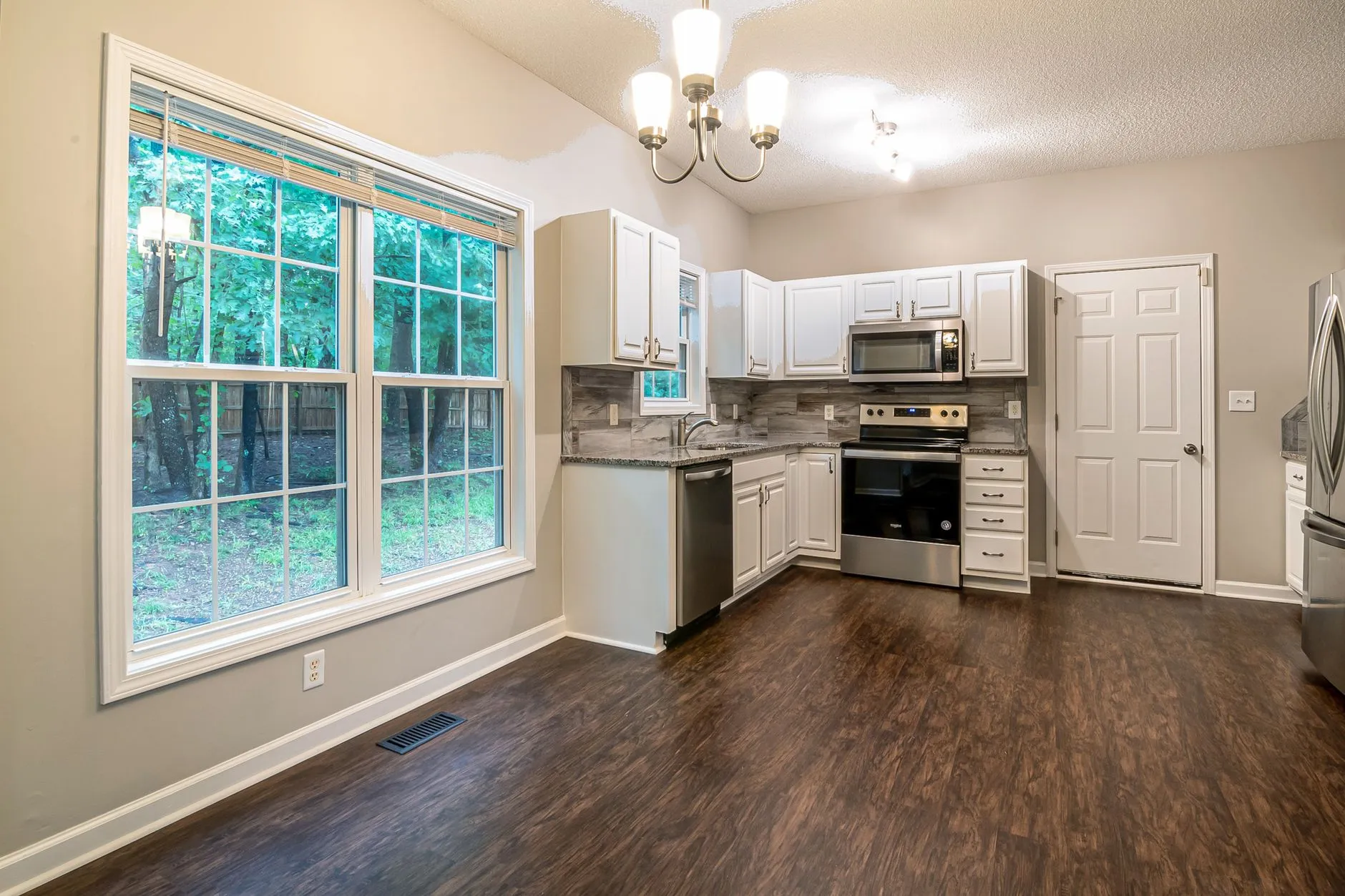 A kitchen with white cabinets and a dark wood-look plank floor